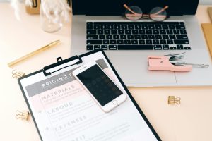 A stylish workspace featuring a laptop, smartphone, clipboard, and stationery essentials.